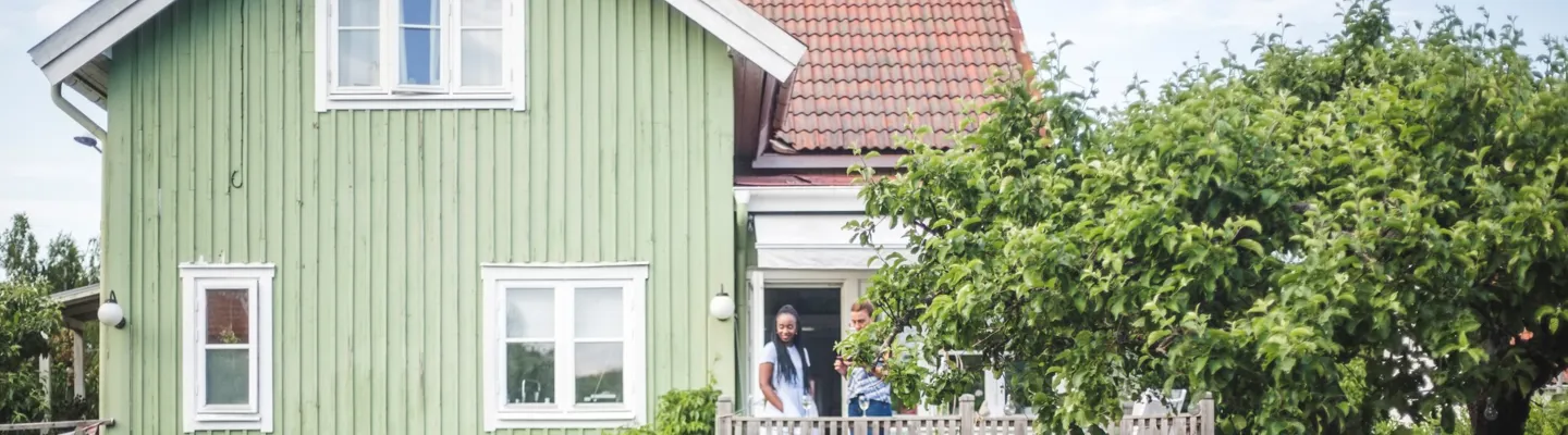 Par pratar på veranda utanför grönt hus