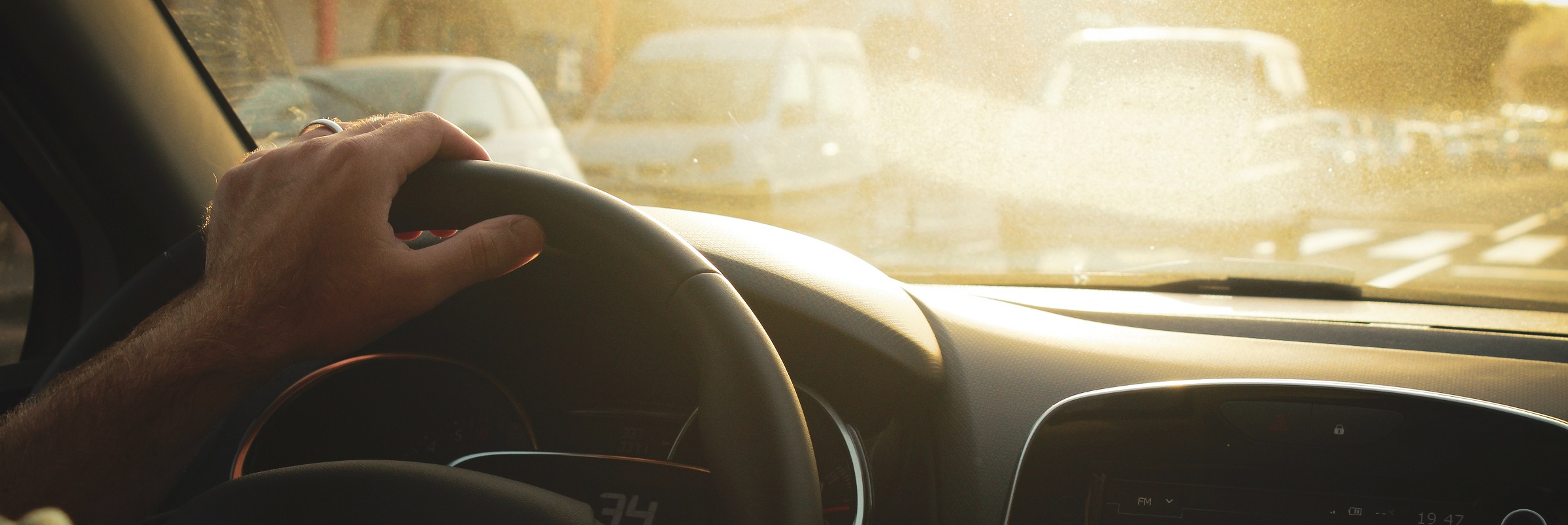 Person kör bil och håller handen på ratten i motljus