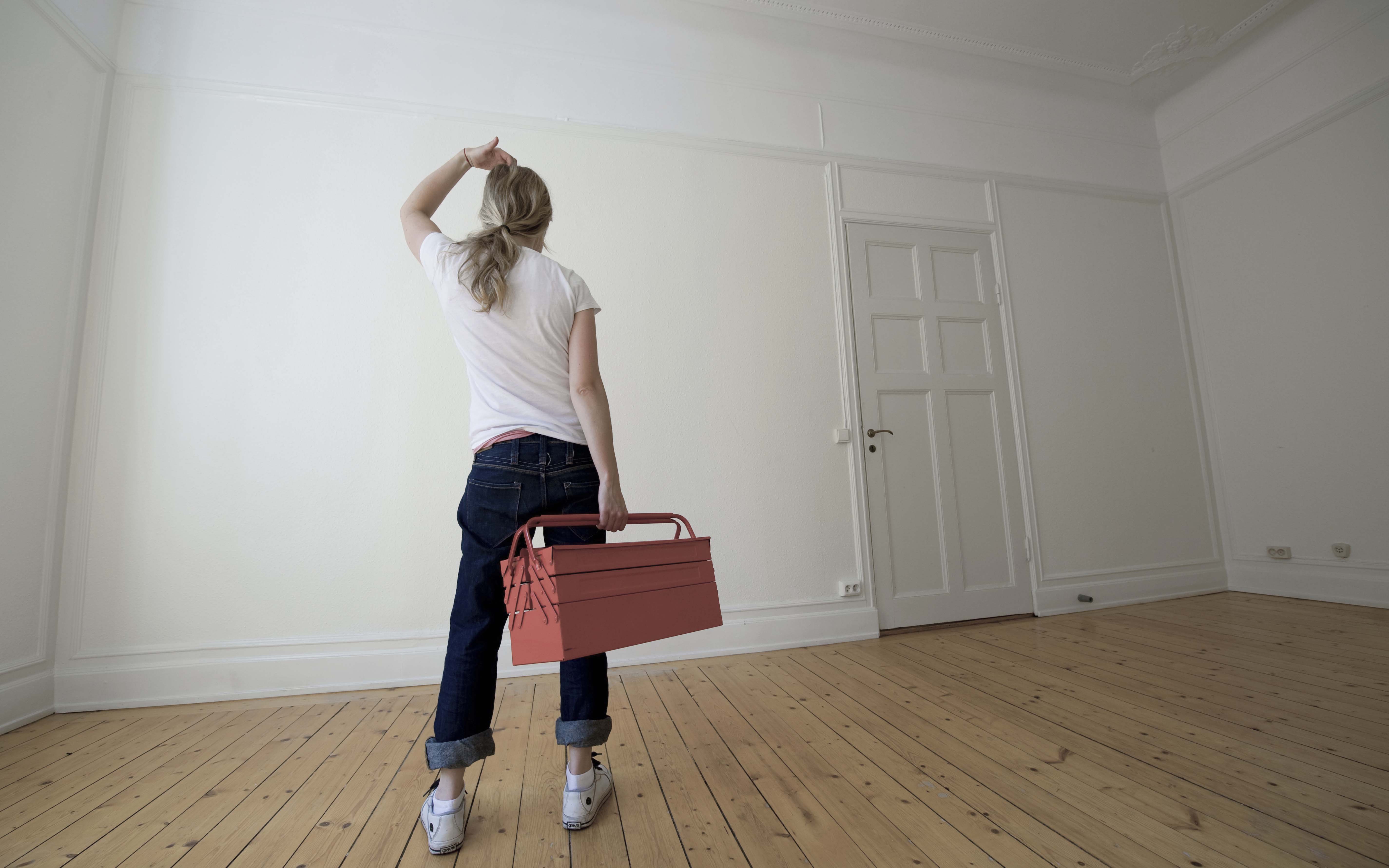 Kvinna med verktygslåda tittar på vägg