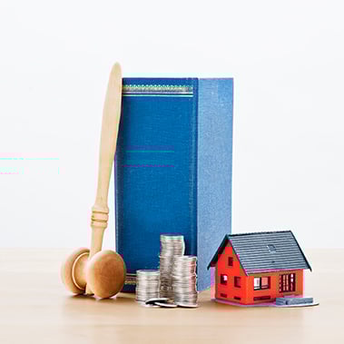 Lagbok och klubba tilssamans med rött miniatyrhus och mynt