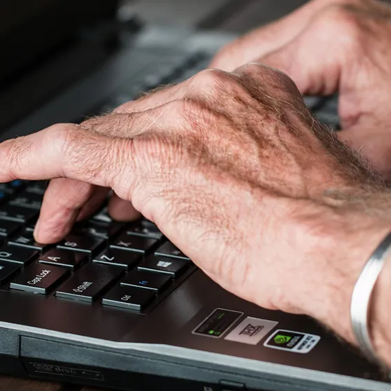 Händer på gammal man skriver på lap top