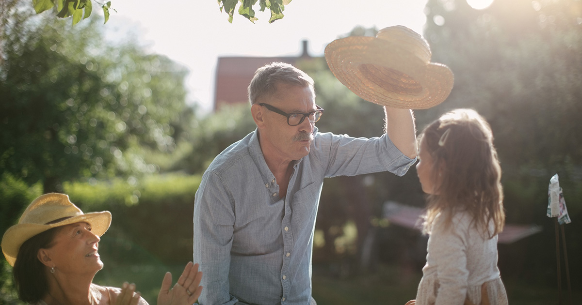 Äldre man håller i hatt och leker med flicka
