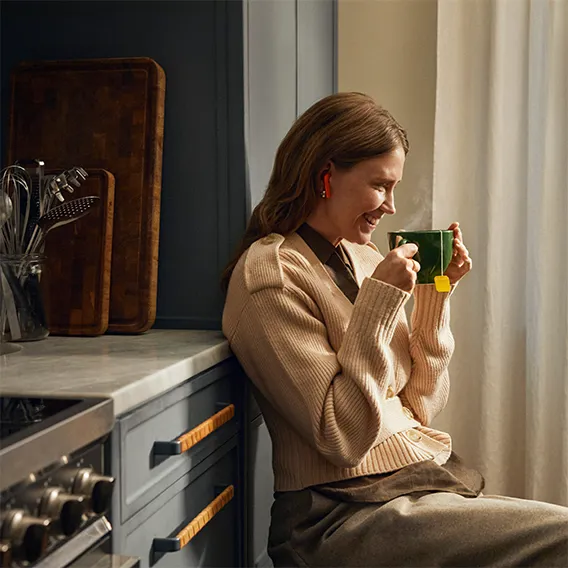 Glad kvinna som sitter i köket och dricker te och lyssnar på ljudbok